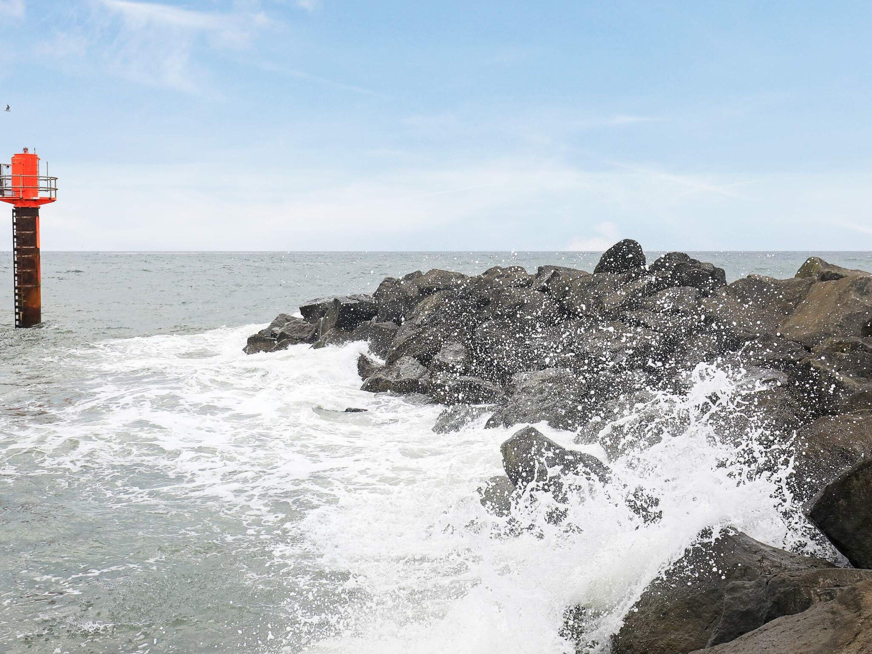 Eine felsige Küste, auf der Wellen brechen, mit einem Leuchtturm im Hintergrund.