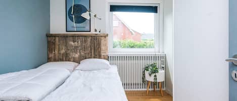 A bedroom with a bed, a radiator, a window, and a framed picture on the wall.