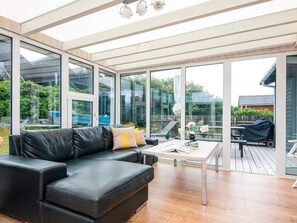 A modern living room with a black leather sofa, a coffee table, and large glass doors leading to an outdoor patio. - 4 Star Holiday Home in Ulfborg (Ulfborg)