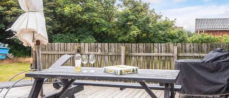 A wooden deck with a picnic table, a barbecue grill, and a covered umbrella.