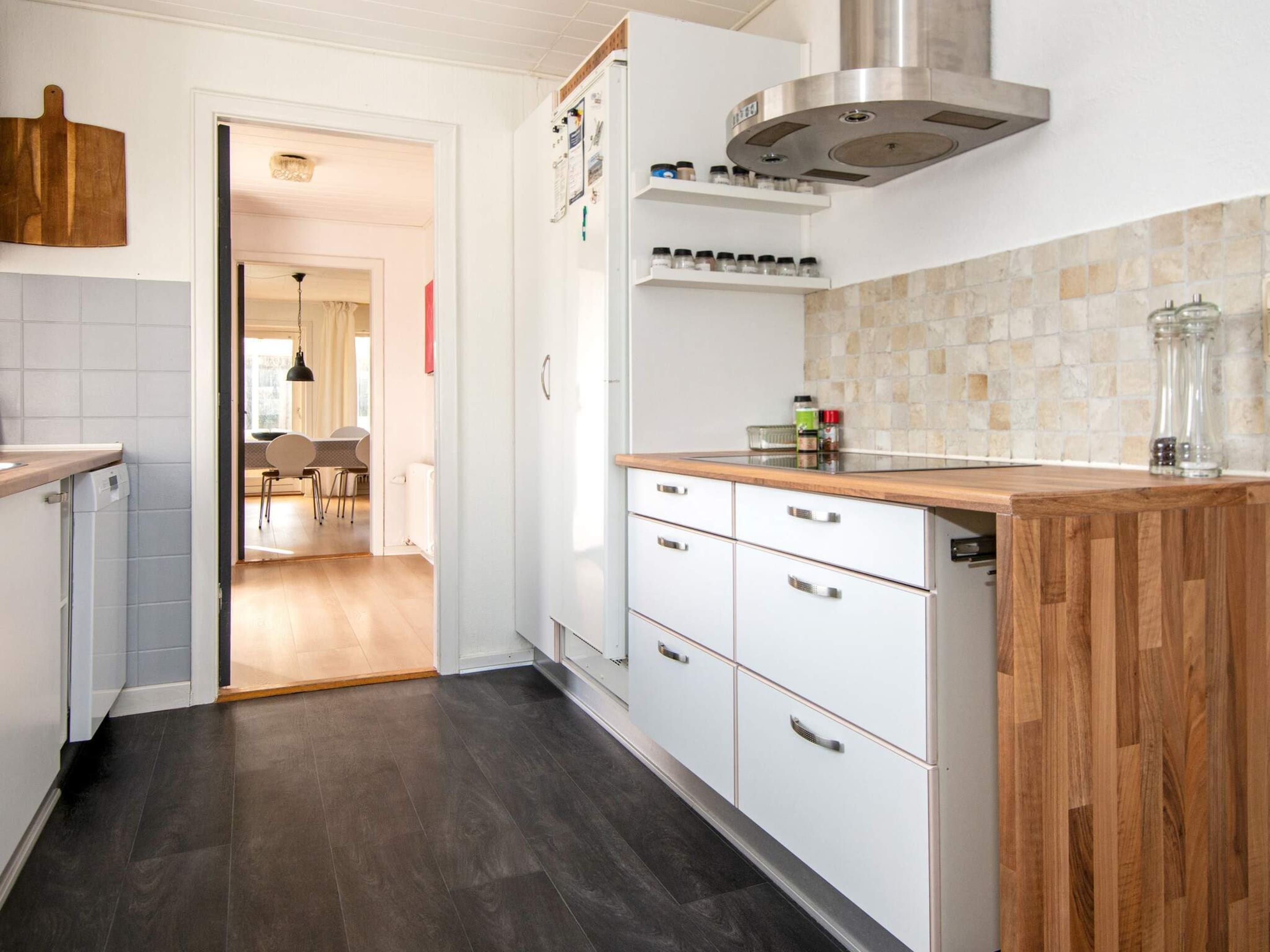 Une cuisine moderne avec des armoires blanches, un plan de travail en bois, une hotte de cuisine en acier inoxydable et un dosseret carrelé.
