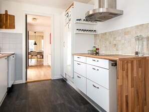A modern kitchen with white cabinets, a wooden countertop, a stainless steel range hood, and a tiled backsplash. - Luxury Spa Retreat in Thorsminde (Ulfborg)