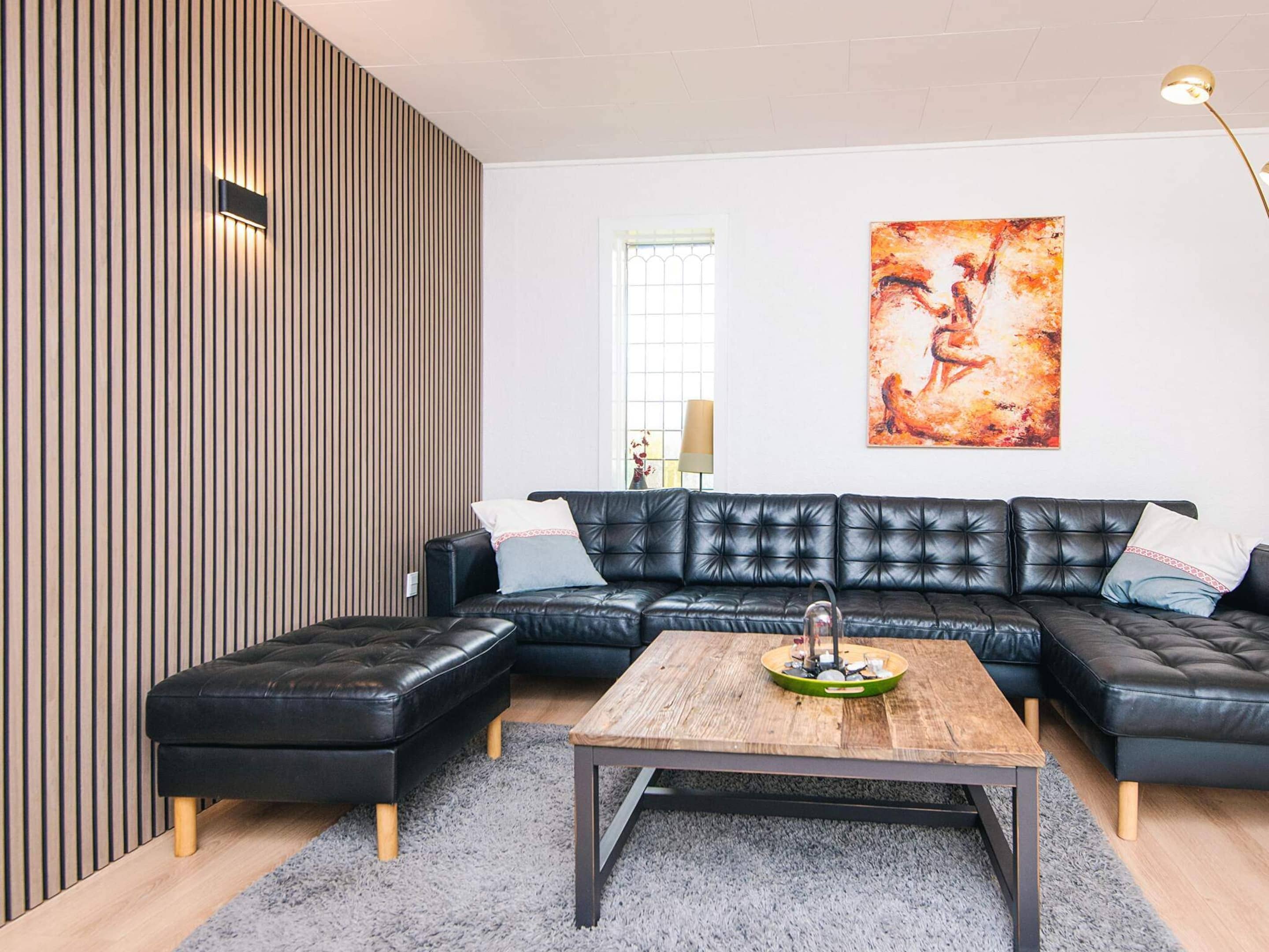 Un salon moderne avec un canapé en cuir noir, une table basse en bois et un tapis à poils longs de couleur grise.