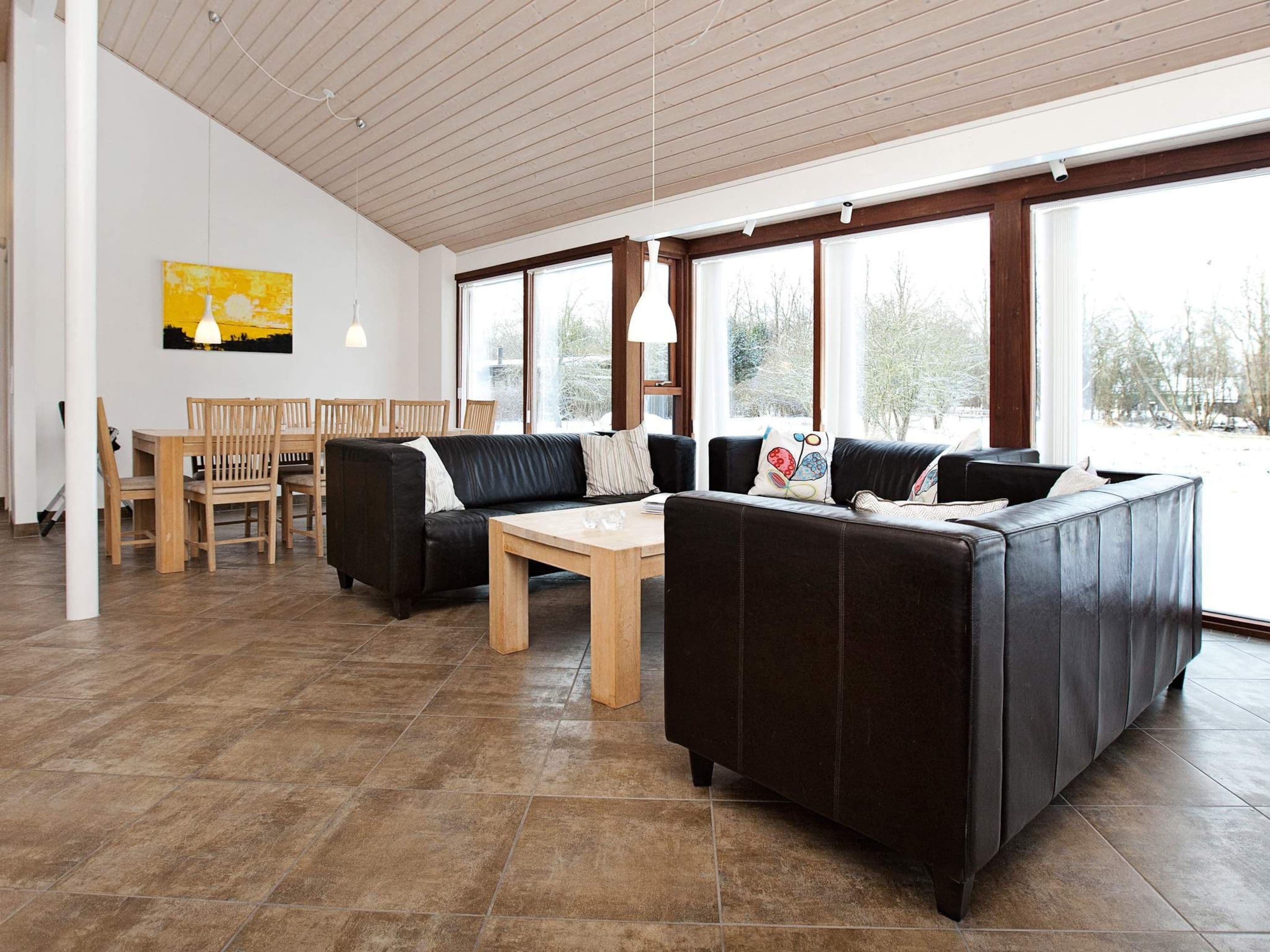 A modern living room with a sectional sofa, a dining table with chairs, and large windows offering a view of the outdoors.
