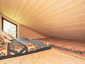 A room with a sloped ceiling, wooden walls, a large window, and a bed with patterned bedding.