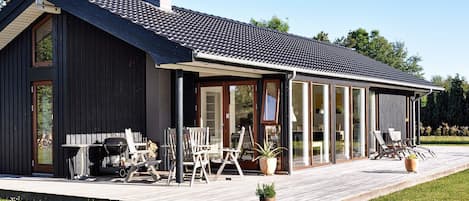 Ein modernes Haus mit überdachter Terrasse, Sitzgelegenheiten im Freien und einer Satellitenschüssel.