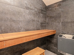 A bathroom with a wooden shelf and bench, a towel rack, and a water heater. - 4 Star Holiday Home in Dannemare (Dannemare)