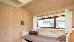 Une chambre avec un lit simple, un plafond en bois, une fenêtre avec des rideaux et un tableau au mur.