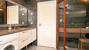 Une salle de bain moderne avec un grand miroir, un lave-linge, un tabouret en bois et une cabine de douche en verre.