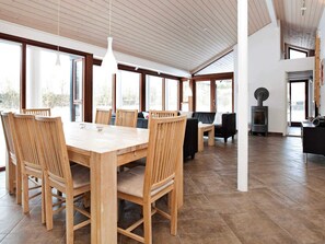 A spacious dining area with a wooden table and chairs, large windows, and a wood-burning stove.