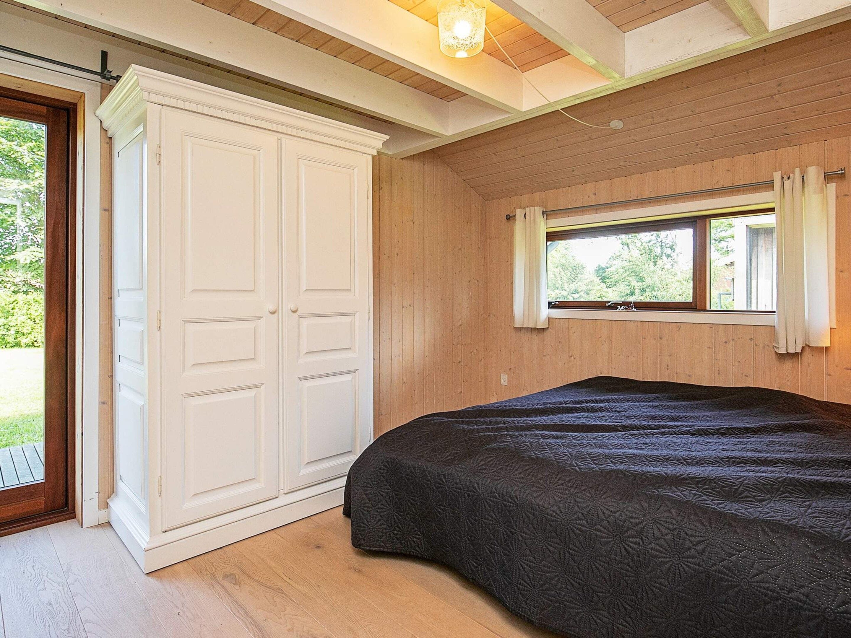 Une chambre à coucher avec un grand lit, une armoire et une fenêtre avec des rideaux.