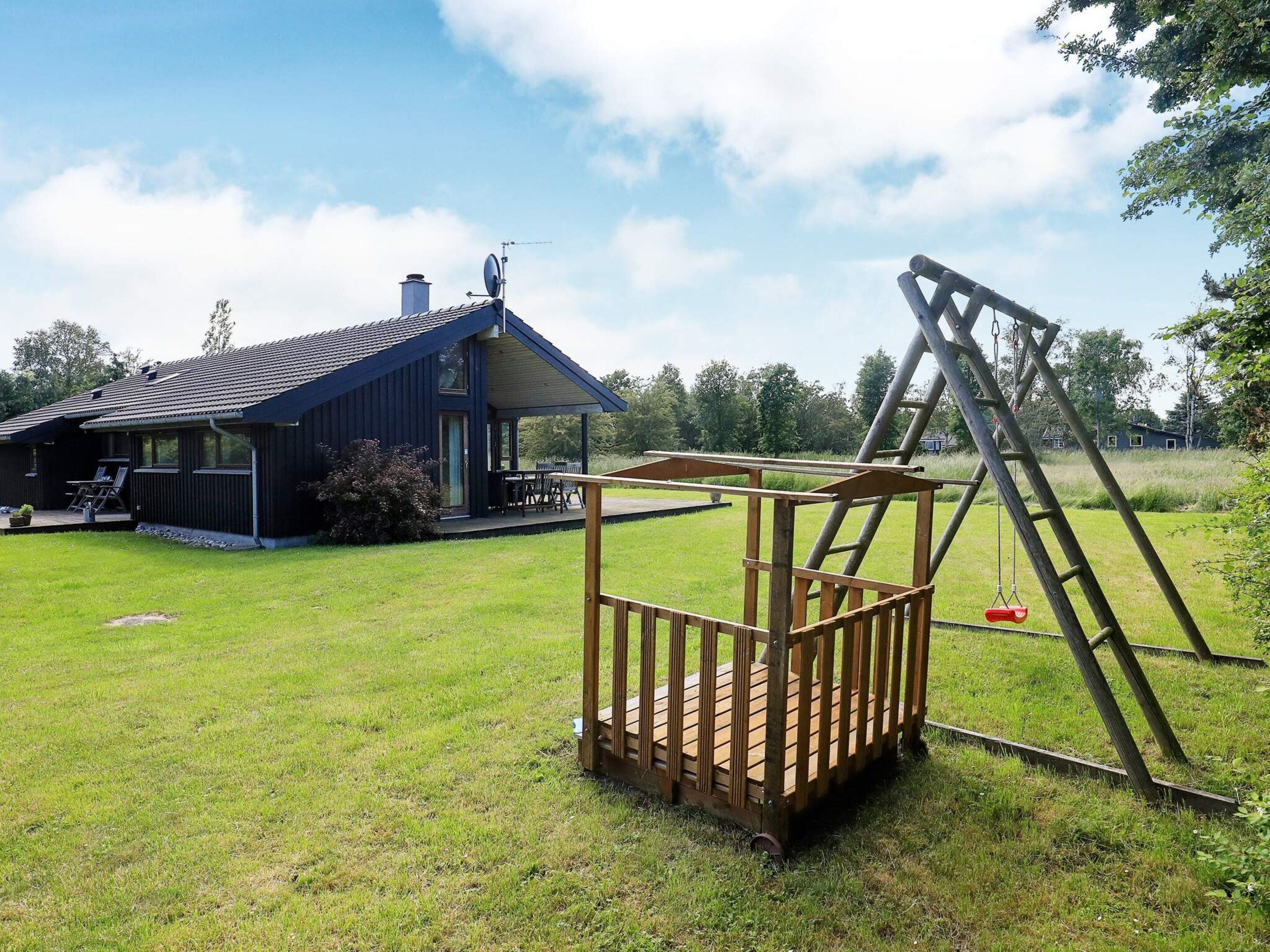 Een houten speeltoestel in een gazon met een huis op de achtergrond.