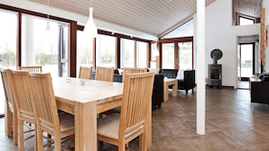 Un vaste espace dédié à la salle à manger, avec une table et des chaises en bois, de grandes fenêtres et un poêle à bois.