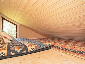 A cozy attic bedroom with a sloped ceiling, a large window, and a bed with patterned bedding.