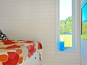 Une chambre à coucher avec un lit, une fenêtre donnant sur des arbres et un objet bleu posé sur le rebord de la fenêtre.