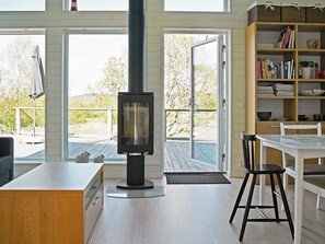 Een modern interieur met een houtkachel, een eethoek met een witte tafel en stoelen, en een boekenkast vol boeken en decoratieve objecten.