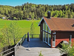 A wooden deck with a view of a green field and a red-roofed building. - Holiday Home in Henån (Henån)