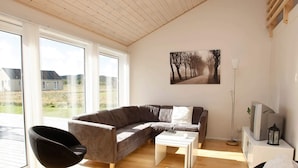 A modern living room with a curved sofa, a black chair, a coffee table, and a TV on a stand. - 10 Person Holiday Home in Brovst (Brovst)