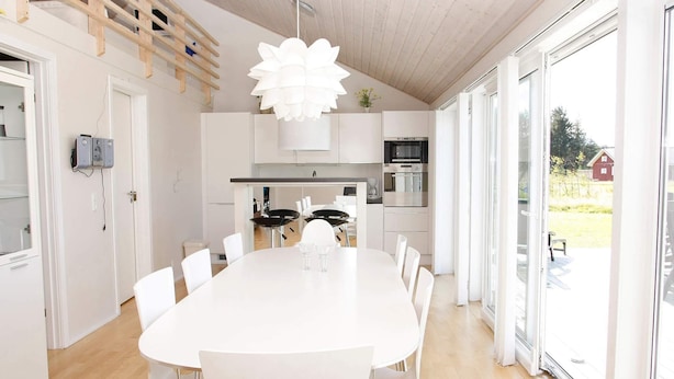 A modern kitchen with white cabinets, stainless steel appliances, and a large dining table with chairs. - 10 Person Holiday Home in Brovst (Brovst)