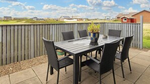 Eine Terrass mit Tisch, Stühlen, einem Blumentopf und Blick auf Häuser im Hintergrund.
