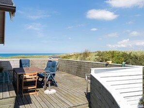 A wooden deck with a table and chairs, overlooking a beach and dunes.