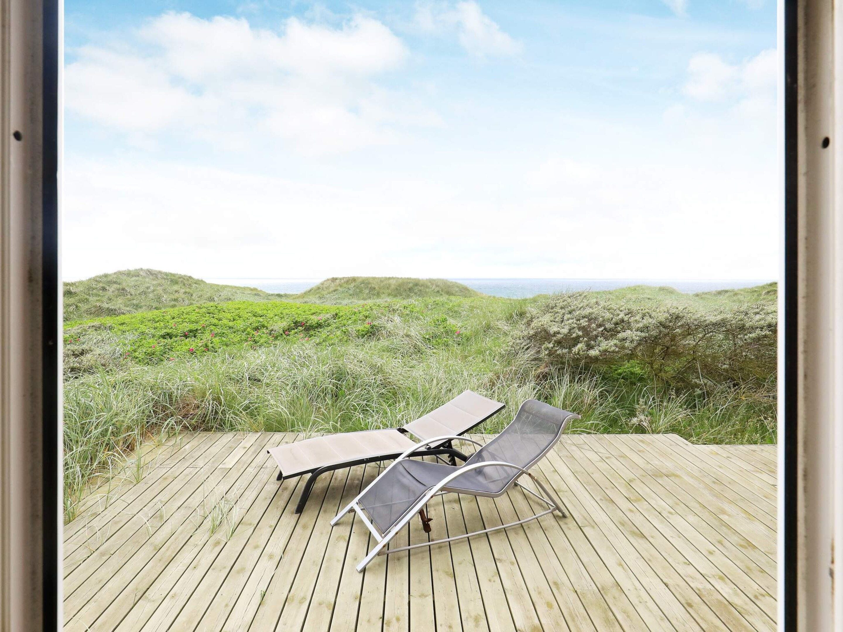 A wooden deck with two lounge chairs facing a coastal landscape.