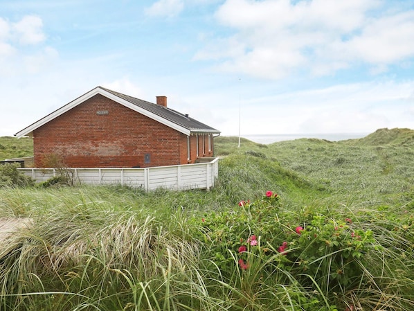 A brick building with a sloped roof, surrounded by grassy terrain and a clear sky.
