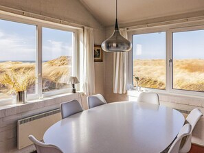 Une pièce dotée d’une grande table ronde, de chaises blanches, d’un luminaire suspendu et de grandes fenêtres donnant sur un champ.