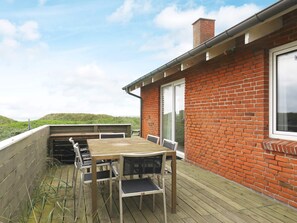 Une terrasse en bois avec une table et des chaises, un mur en briques et une fenêtre.
