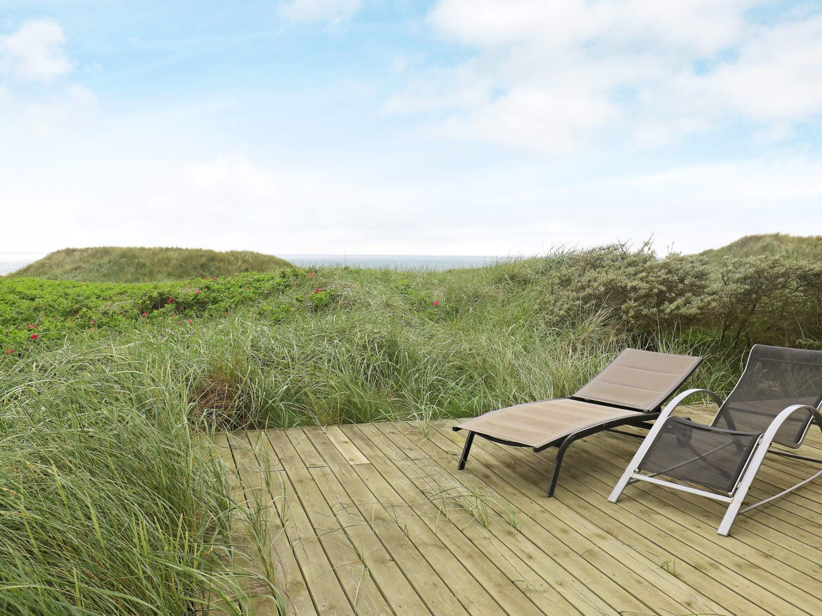 A wooden deck with two lounge chairs facing a coastal landscape.