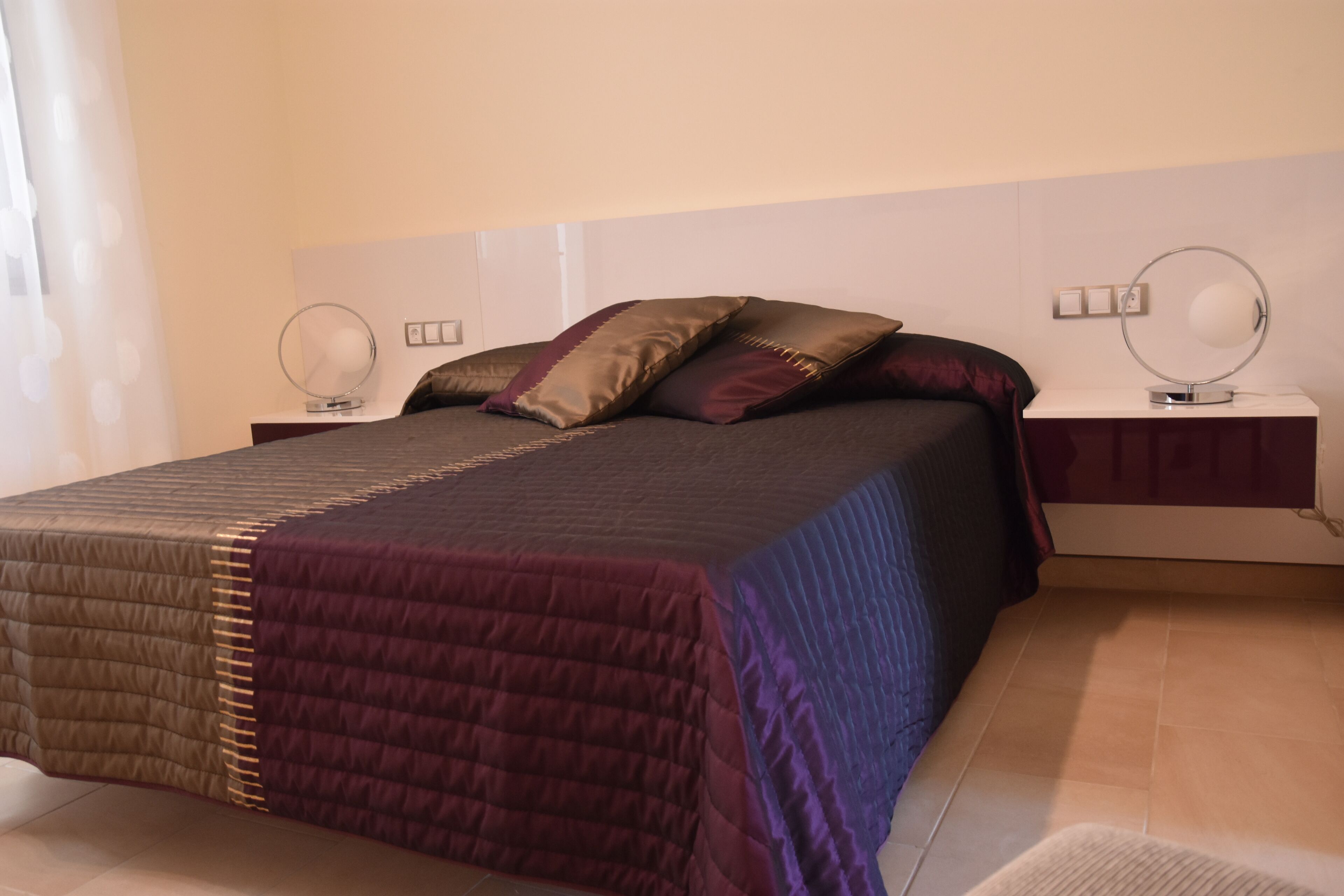 A bedroom with a bed, two bedside tables, and a mirror on each table.