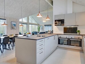 Une cuisine moderne dotée d’un îlot central, d’appareils électroménagers en acier inoxydable et de luminaires suspendus.