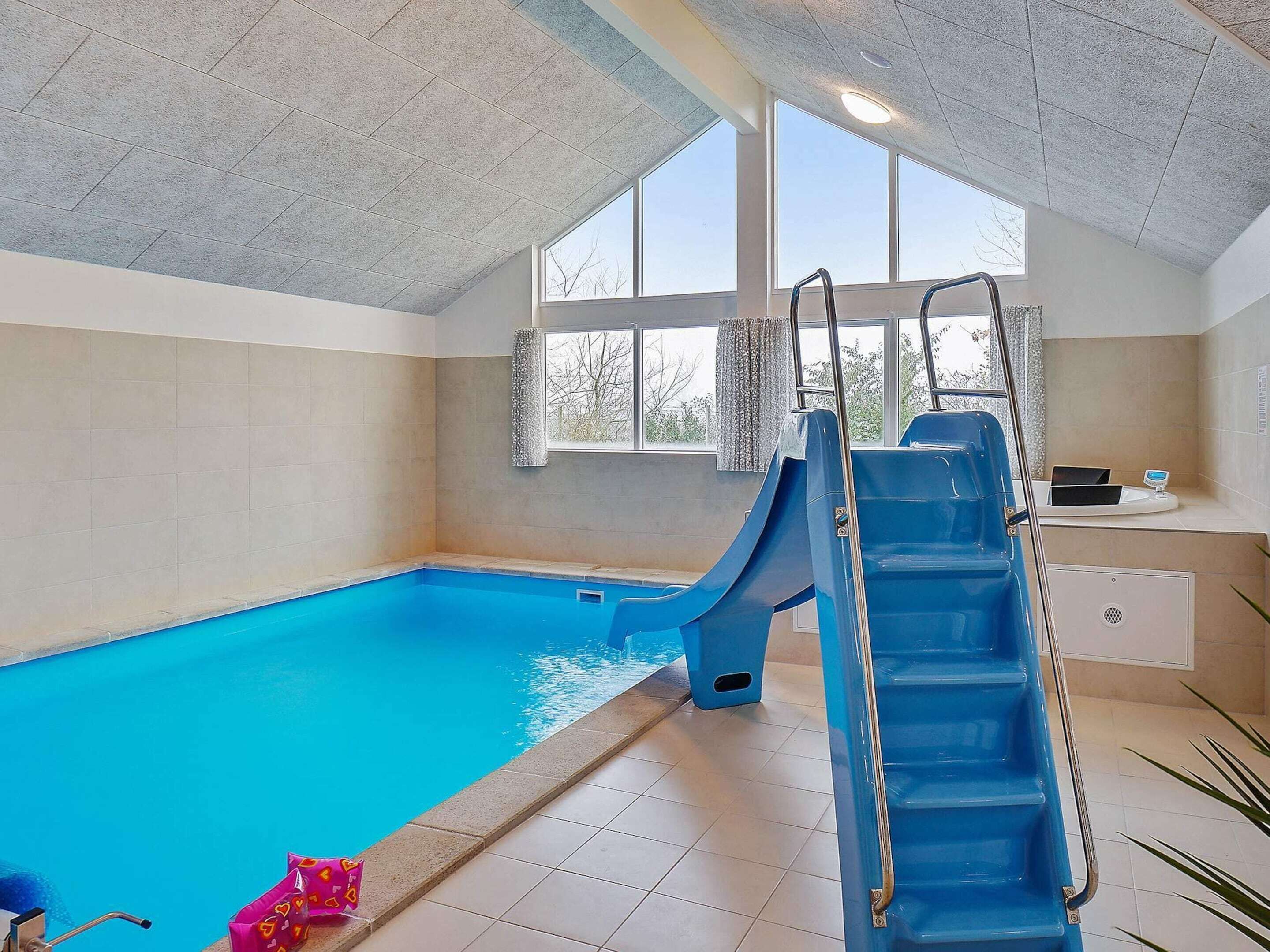An indoor swimming pool with a blue slide, a window, and a small sink area.