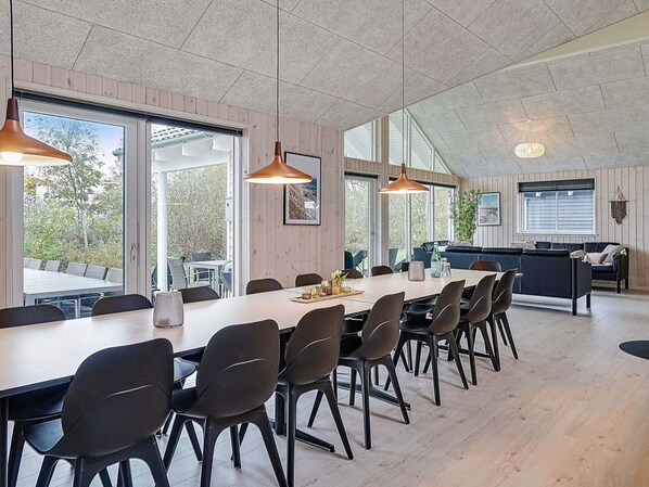 A modern dining area with a long table, black chairs, pendant lighting, and large windows offering a view of the outdoors. - Holiday Home in Kappeln (Kappeln)