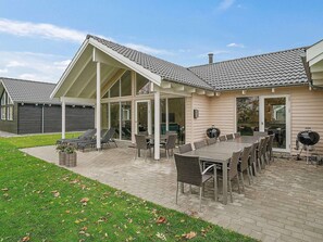 Une terrasse couverte, aménagée avec du mobilier d’extérieur, un barbecue et offrant une vue sur la maison.