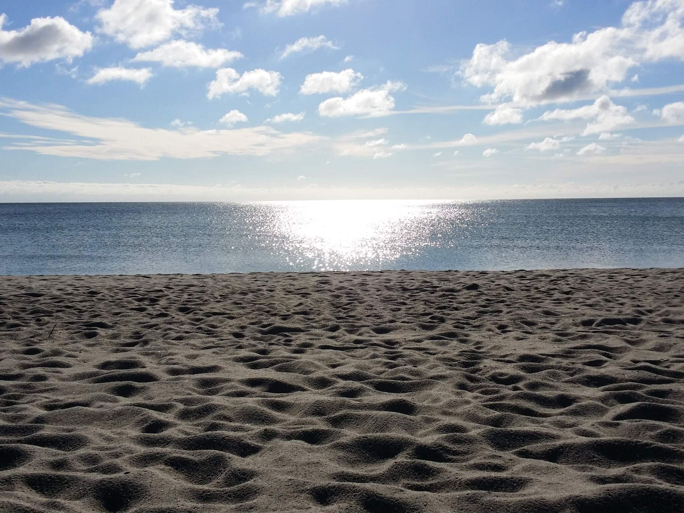 Une plage avec un ciel dégagé et le soleil se reflétant sur l’eau.
