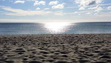 A beach with a clear sky and the sun reflecting on the water.