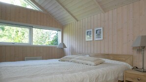 A bedroom with a large bed, wooden walls, a window, and two wall-mounted lamps. - 5 Star Holiday Home in Vaeggerlose (Vaeggerlose)