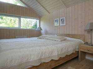 A bedroom with a large bed, wooden walls, a window, and two wall-mounted lamps. - 5 Star Holiday Home in Vaeggerlose (Vaeggerlose)