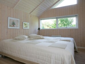 Quarto com cama grande, paredes de madeira, janela vista para árvores e duas fotos emolduradas na parede.