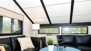 En modern inredning med en svart lädersoffa, ett runt soffbord i trä och en krukväxt.