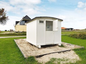 A small, white, single-room structure with a door and a window, situated on a grassy area with a paved path leading to it.