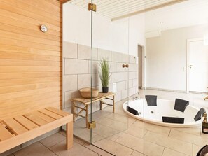 Une salle de spa moderne avec un banc en bois, une petite table ornée d’une plante et une baignoire blanche.