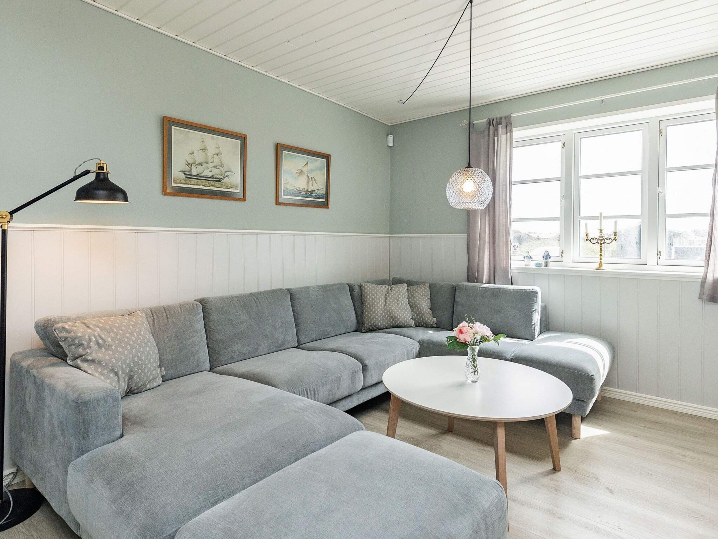 A modern living room with a grey sectional sofa, a round coffee table, and two framed maritime paintings on the wall.