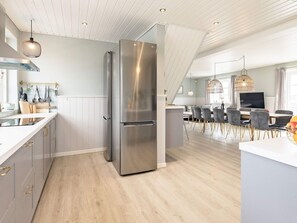 Une cuisine moderne dotée d’un réfrigérateur en acier inoxydable, d’un plancher en bois et d’un coin repas avec des chaises et une table grises.
