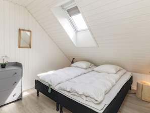 Un dormitorio con techo inclinado, una cama con ropa de cama blanca, un aparador y un espejo en la pared.
