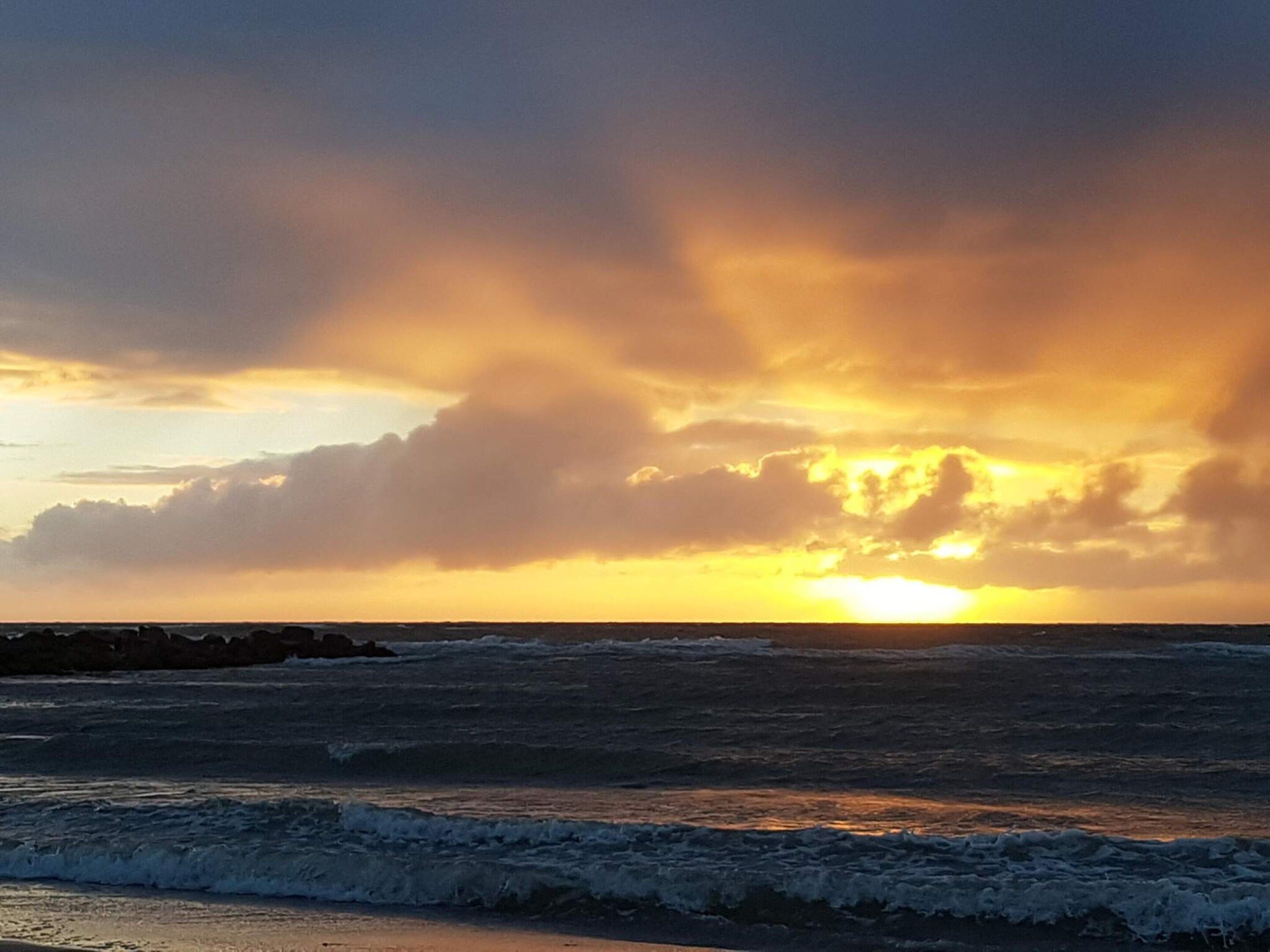 Un coucher de soleil sur l’océan, avec des vagues qui déferlent sur la plage.