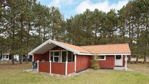 Un petit bâtiment d’un seul étage, à l’extérieur rouge et doté d’un toit en tuiles, entouré d’une pelouse et d’arbres.