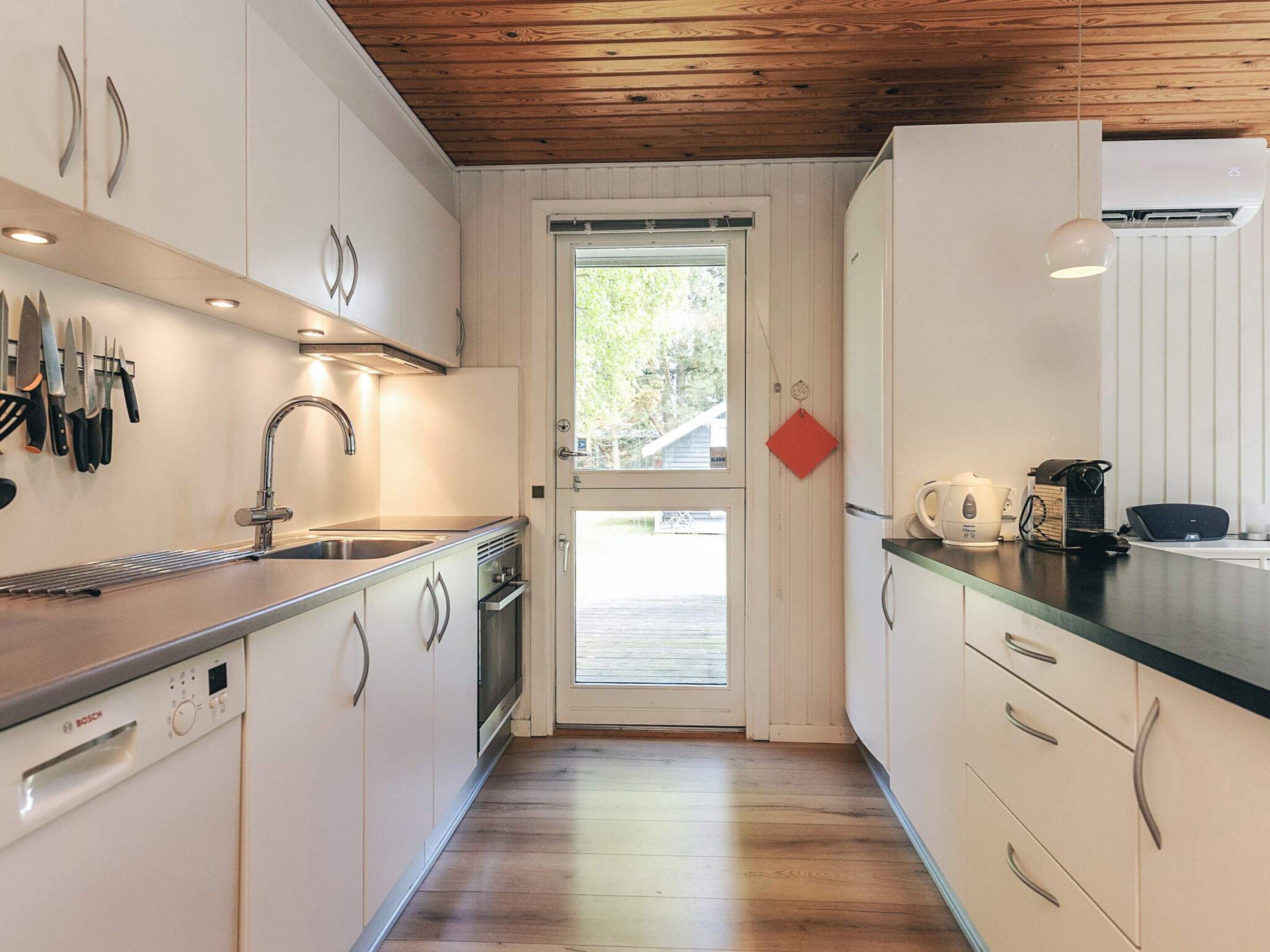 A kitchen with white cabinets, a Bosch dishwasher, a stainless steel sink, and a wooden ceiling.