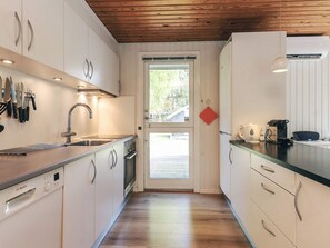 Eine Küche mit weißen Schränken, einem Geschirrspüler von Bosch, einer Edelstahlspüle und einer Holzbalkendecke.